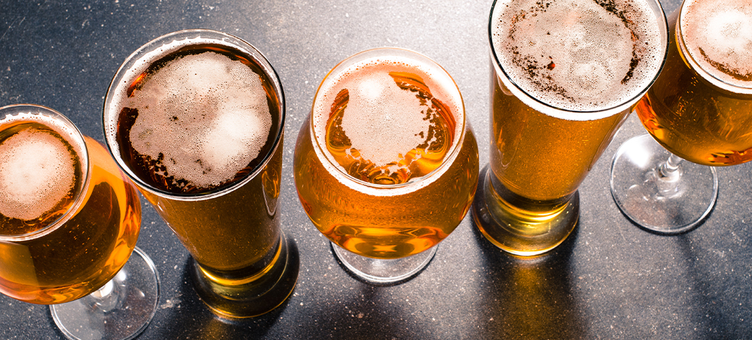 Five golden West Coast IPAs with foamy heads in a row, highlighting malt richness and visual diversity in craft beer.