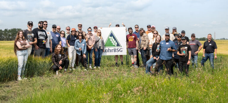 Group of professional brewers stand in a field of barley next to a RahrBSG sign