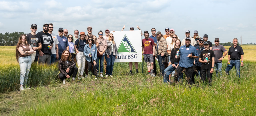 Group of professional brewers stand in a field of barley next to a RahrBSG sign