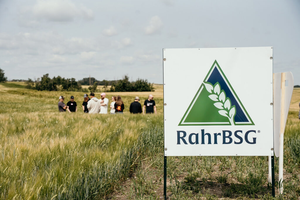 RahrBSG sign in foreground of barley field with brewers in the background